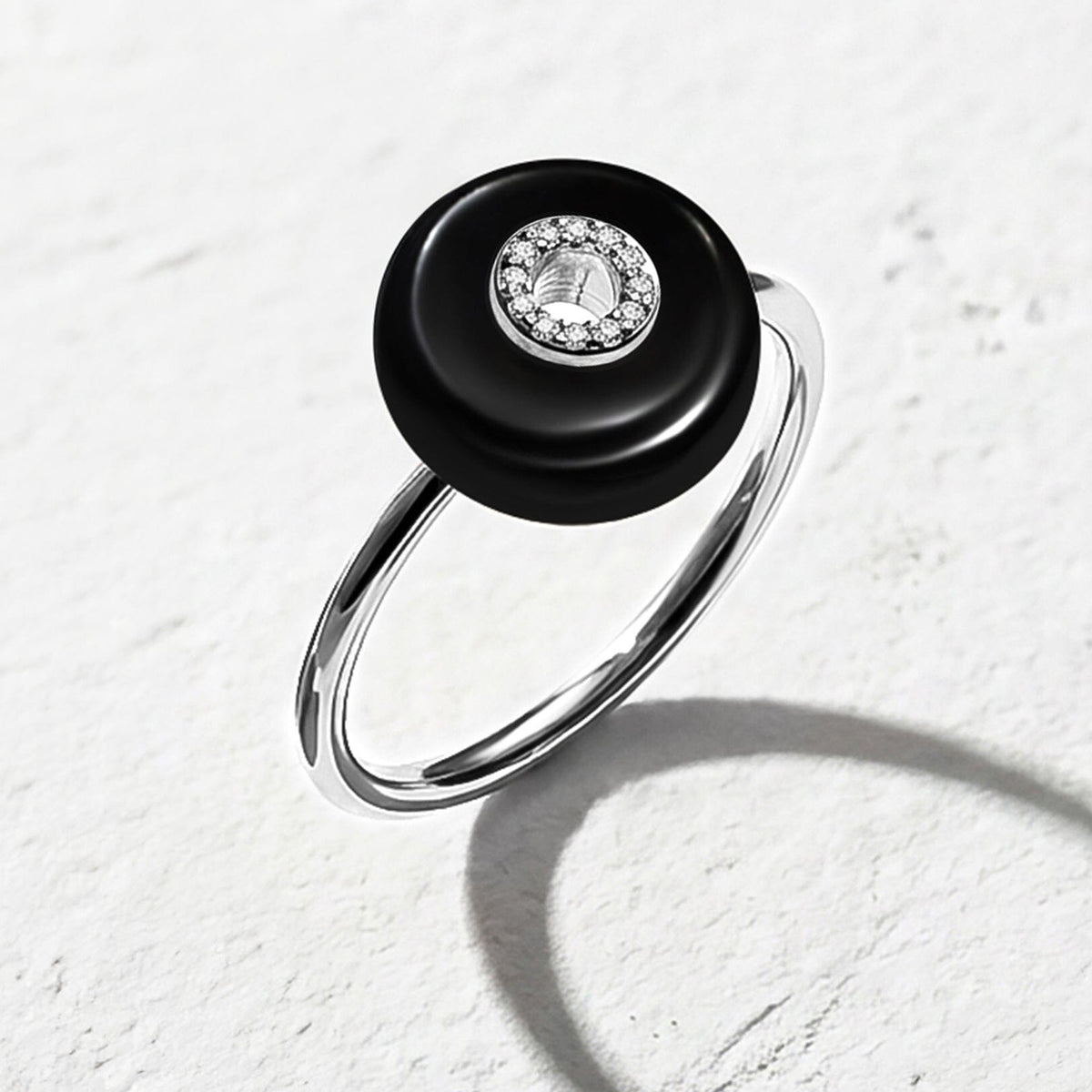 A silver band curves below a glossy black stone with clear center accents on a pale textured tabletop.