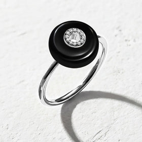 A silver band curves below a glossy black stone with clear center accents on a pale textured tabletop.