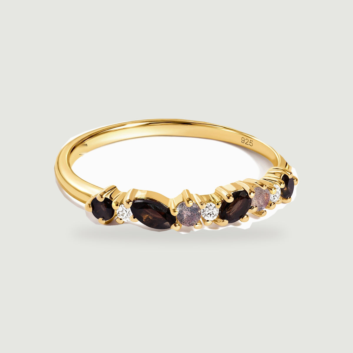 A yellow gold vermeil ring with dark faceted stones and clear round accents rests on a light gray background.