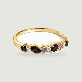 A yellow gold vermeil ring with dark faceted stones and clear round accents rests on a light gray background.