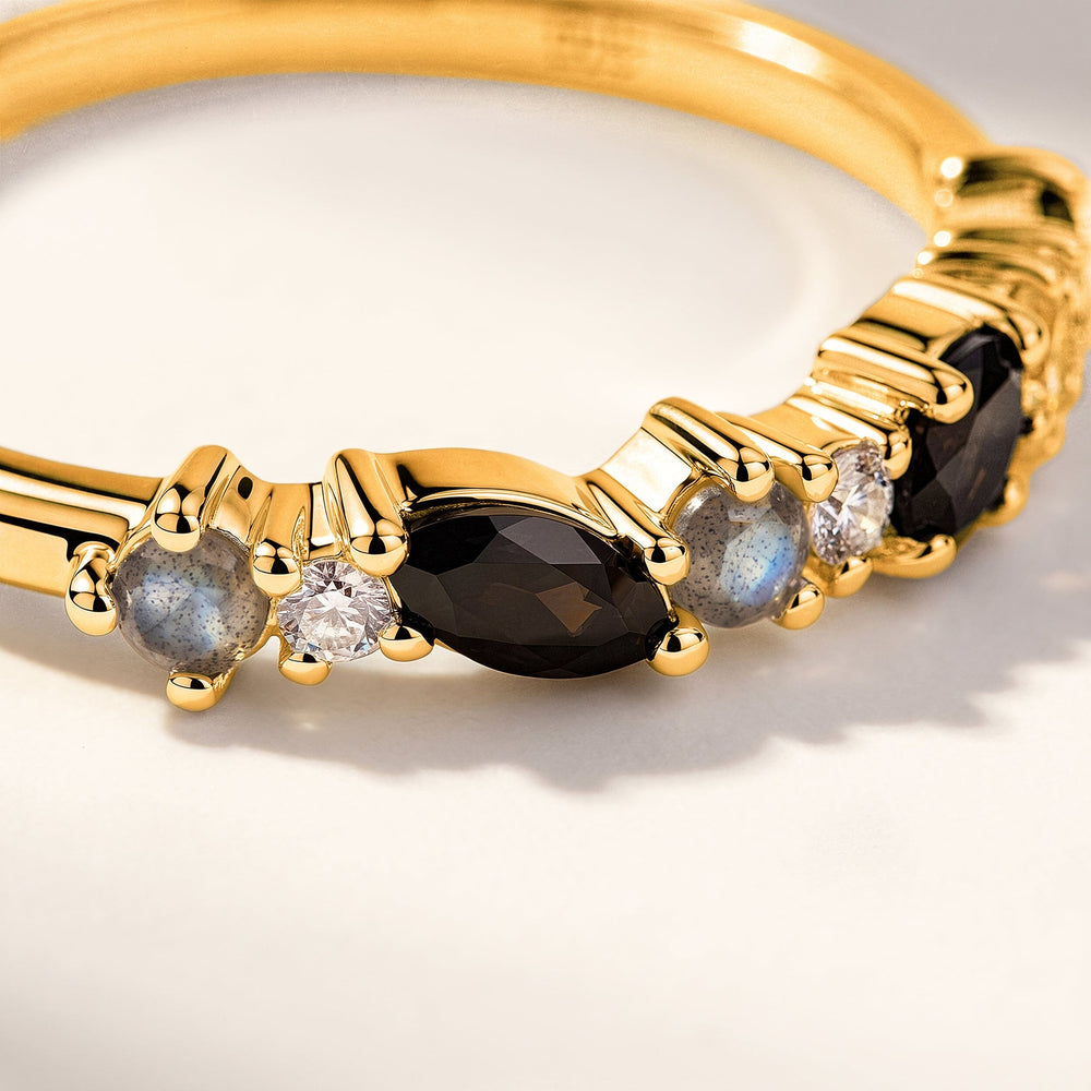 A close view shows yellow gold prongs around a dark marquise stone, clear round stones and blue gray accents.