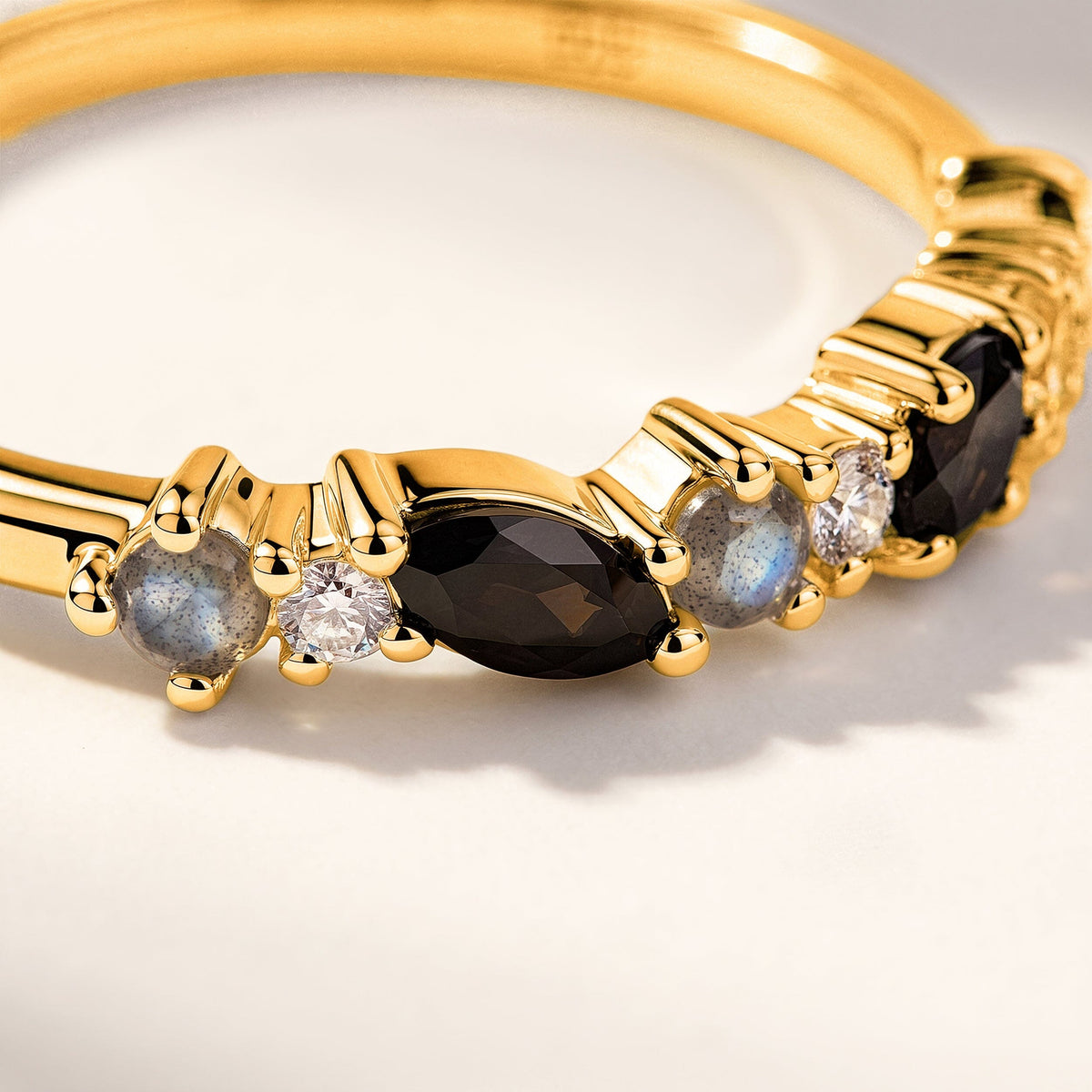 A close view shows yellow gold prongs around a dark marquise stone, clear round stones and blue gray accents.