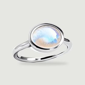 A polished sterling silver ring with an oval blue-flashing moonstone stands at an angle on a light gray surface.