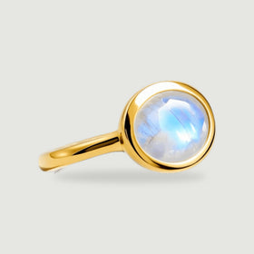 A yellow gold vermeil ring presents its oval moonstone and curved band against a pale gray background.