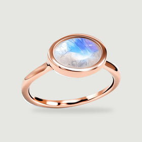 A rose gold vermeil ring shows a blue-flashing oval moonstone above its rounded band on light gray.