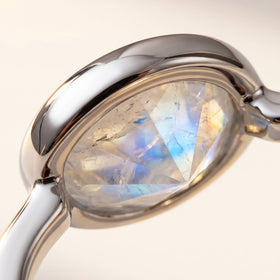A close view reveals pale blue flashes and natural inclusions within an oval moonstone held by a polished silver bezel.