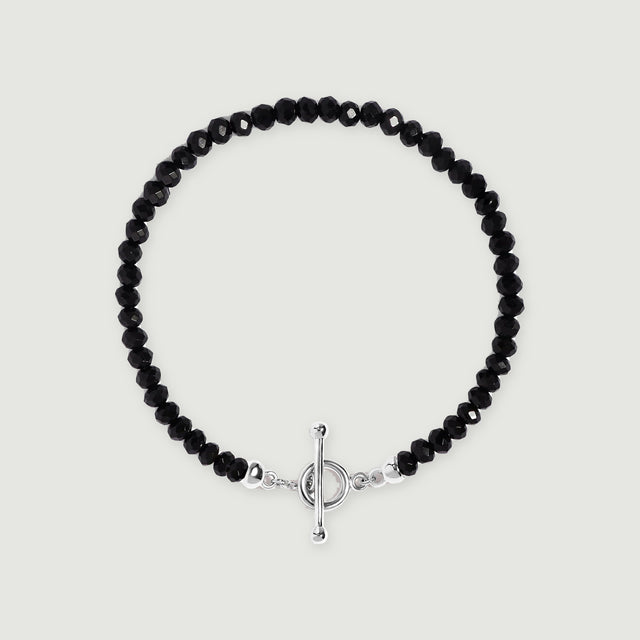 Faceted black obsidian beads form an oval bracelet with a polished silver ring and bar clasp on a light gray background.
