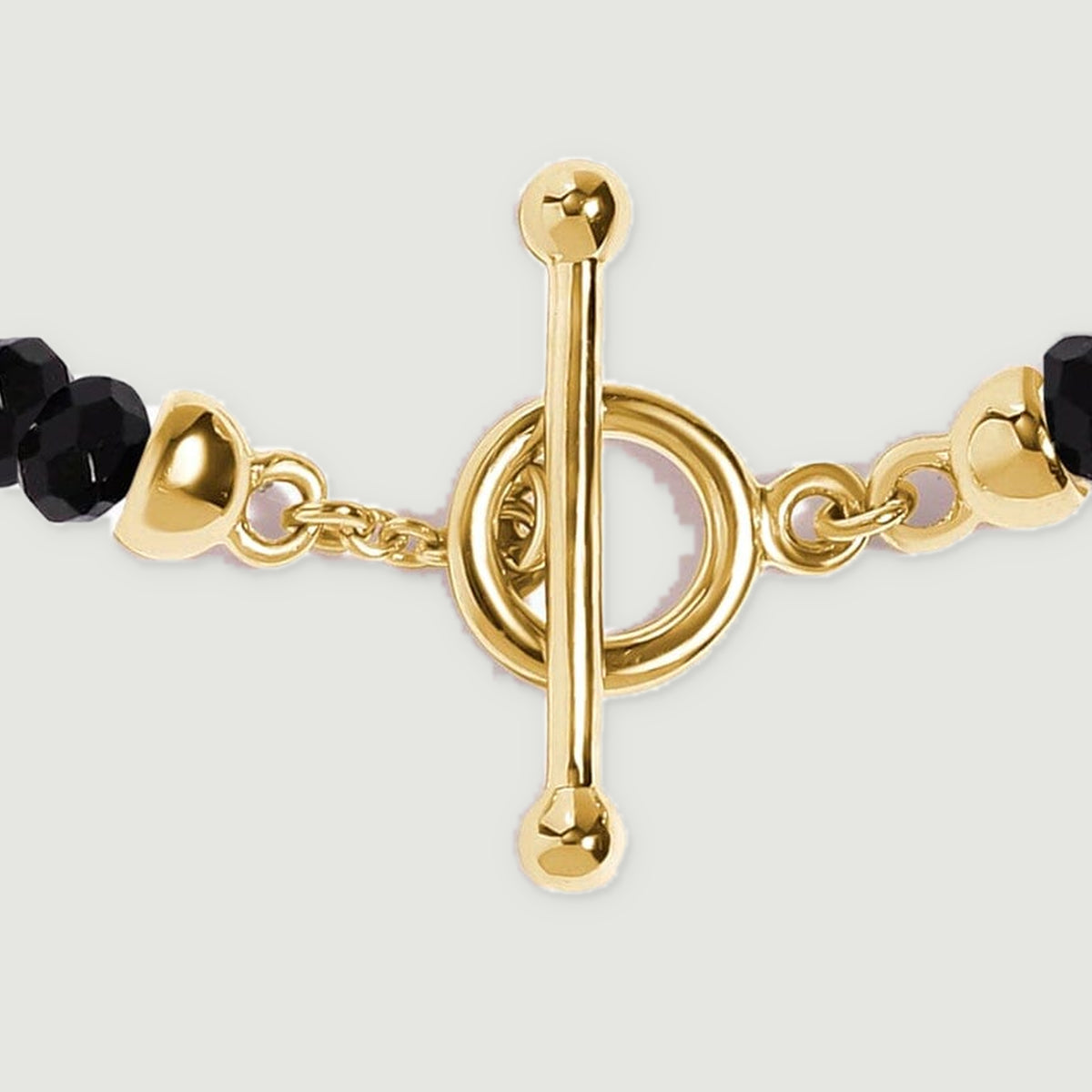Polished yellow gold vermeil clasp details and the ends of the black bead strand fill this close-up.