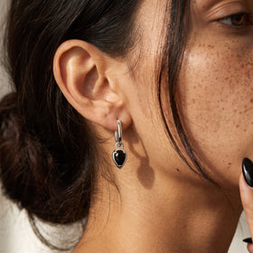 Close-up of a person wearing a pear-shaped black onyx hoop earring beside dark hair.