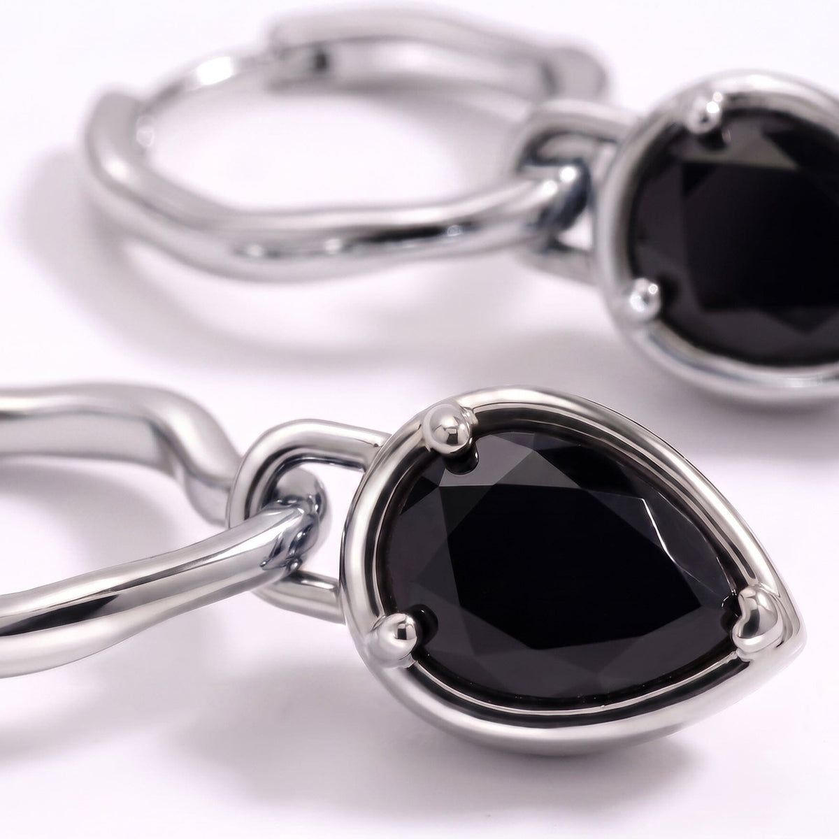 Macro view of a faceted black pear-shaped stone set in a curved hoop earring.
