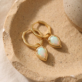 Pair of pear-shaped milky opalescent stone hoop earrings resting on a rustic ceramic dish.