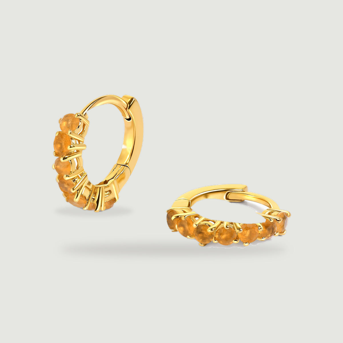 Two yellow gold plated carnelian hoops are centered on a light gray background with soft shadows.