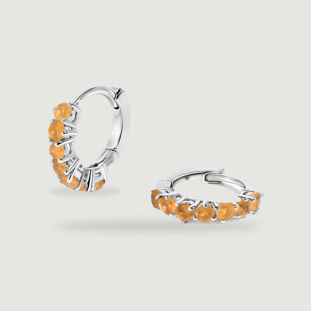 A white rhodium plated hoop pair shows orange round stones and curved polished backs on light gray.