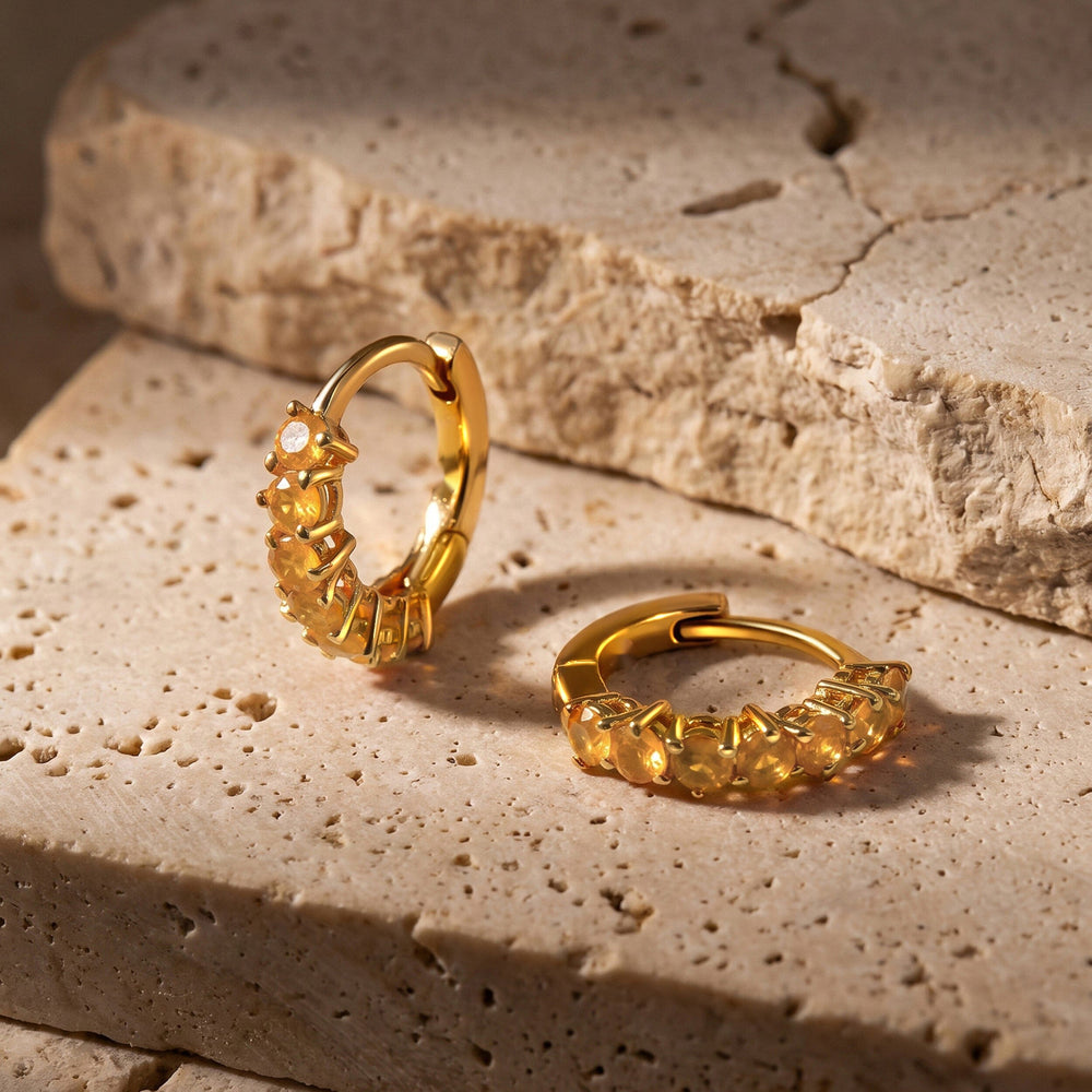Yellow gold plated carnelian hoops rest on a textured pale stone surface, with one hoop standing upright.