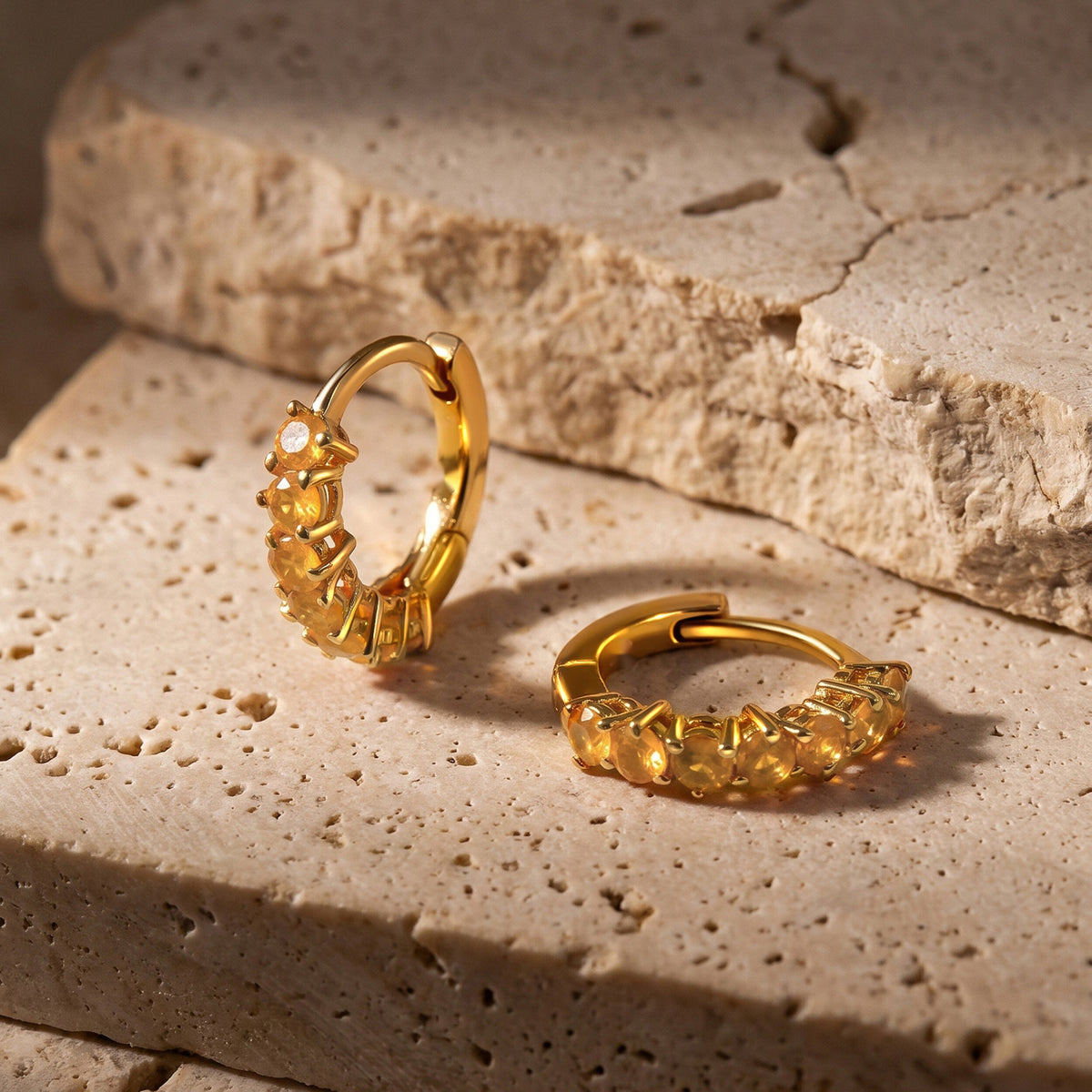 Yellow gold plated carnelian hoops rest on a textured pale stone surface, with one hoop standing upright.