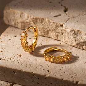 Yellow gold plated carnelian hoops rest on a textured pale stone surface, with one hoop standing upright.