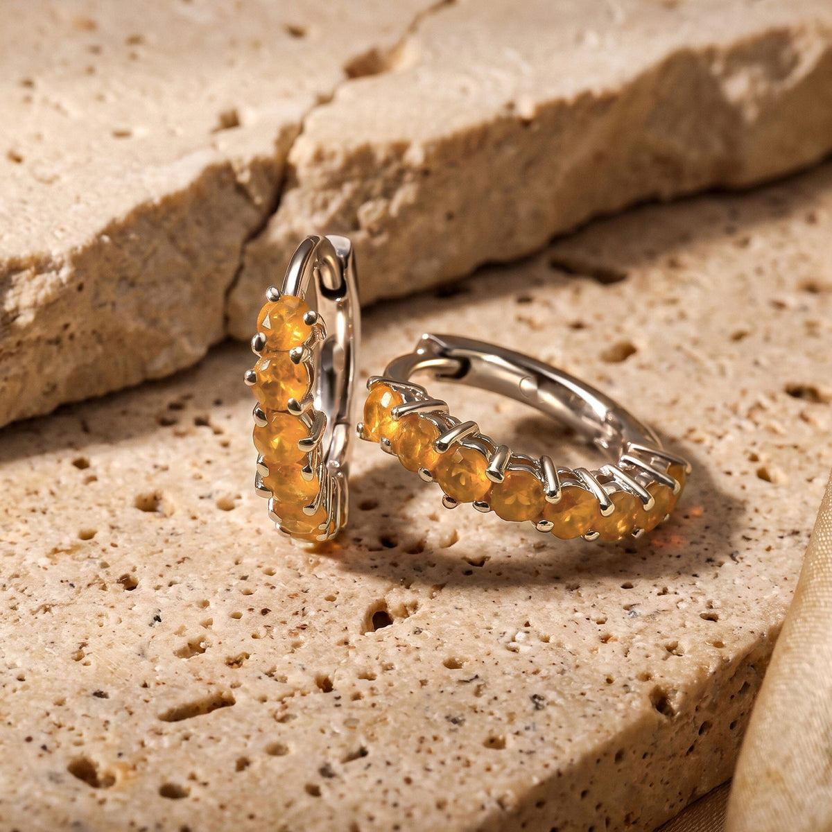 Two white rhodium plated carnelian hoops sit beside a raised edge on a beige stone tabletop.