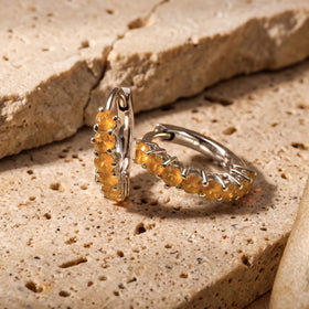 Two white rhodium plated carnelian hoops sit beside a raised edge on a beige stone tabletop.