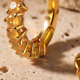 A close view shows orange carnelian facets held by yellow gold plated prongs along a small hoop.