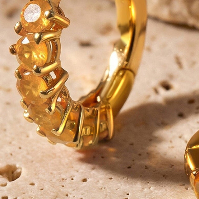 A close view shows orange carnelian facets held by yellow gold plated prongs along a small hoop.