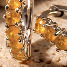 Round orange carnelian stones and white rhodium plated claw settings fill a close view against pale stone.