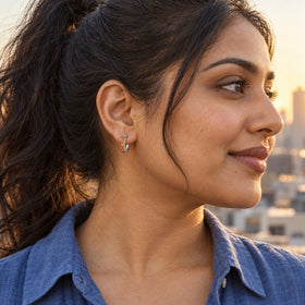 A woman with a dark ponytail wears a white rhodium plated carnelian hoop above a blue shirt with a city skyline behind her.