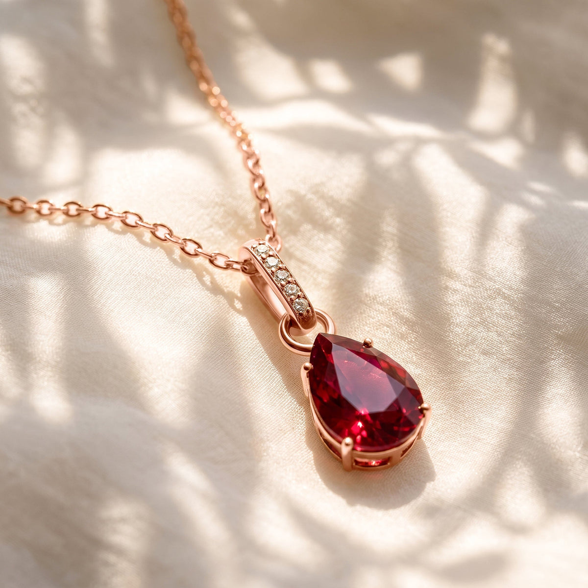 A rose gold ruby necklace lies across softly folded ivory fabric in dappled natural light.