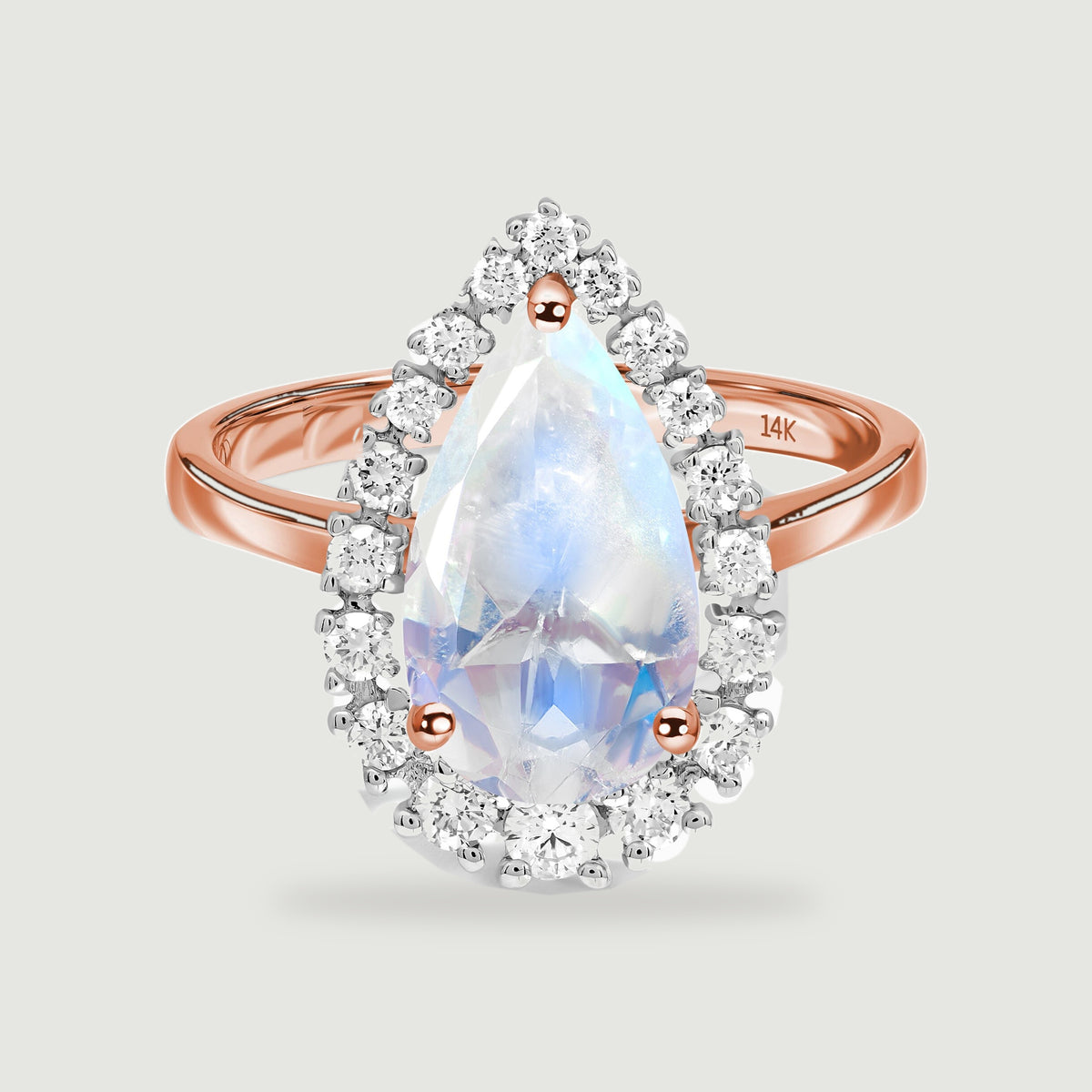 A pear-shaped moonstone is surrounded by round diamonds on a polished rose gold ring against a light gray background.