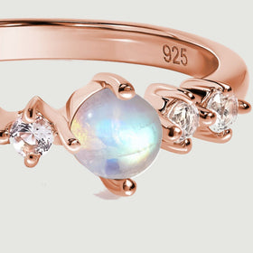 A close view shows blue reflections in the round moonstone beside clear faceted stones and rose gold prongs.