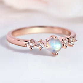 The rose gold moonstone ring lies on a pale tabletop with soft reflections on the band.