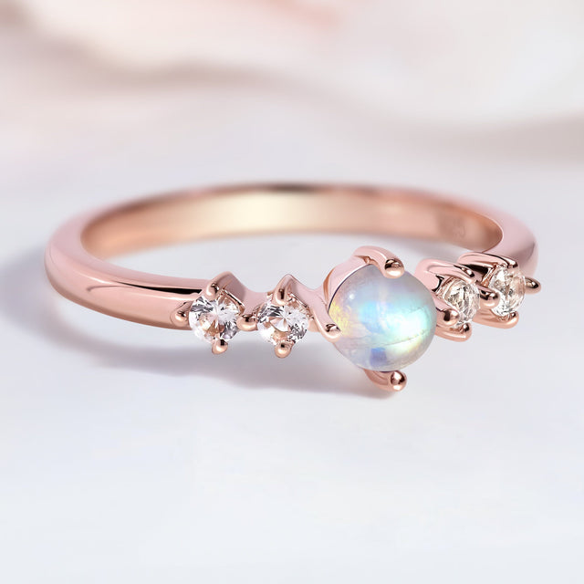 The rose gold moonstone ring lies on a pale tabletop with soft reflections on the band.
