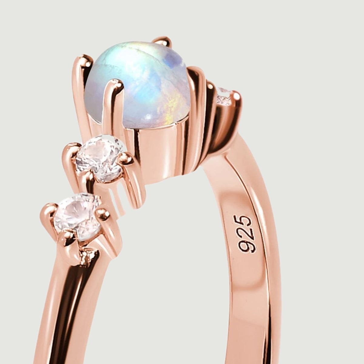 A close side view reveals the rounded moonstone above its rose gold prongs and two clear side stones.