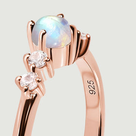 A close side view reveals the rounded moonstone above its rose gold prongs and two clear side stones.