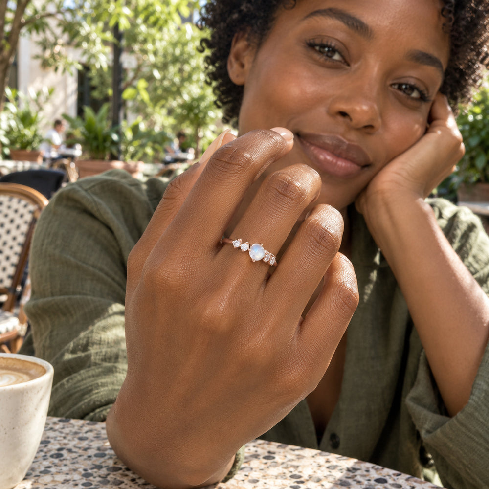 A woman with short curls wears the rose gold moonstone ring at a leafy outdoor cafe.