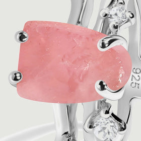 The rough rose quartz center is shown close up with rounded silver prongs and bright accents along the split band.