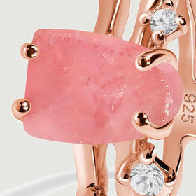 Pink rose quartz sits between rose gold prongs with two small clear accents visible beside the textured stone.