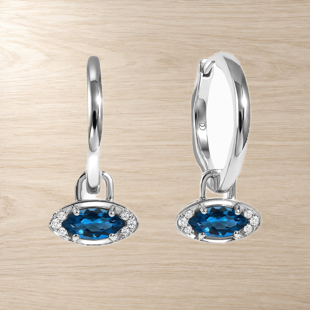 Pair of hoop earrings with blue topaz evil eye charms, shown side by side on pale wood