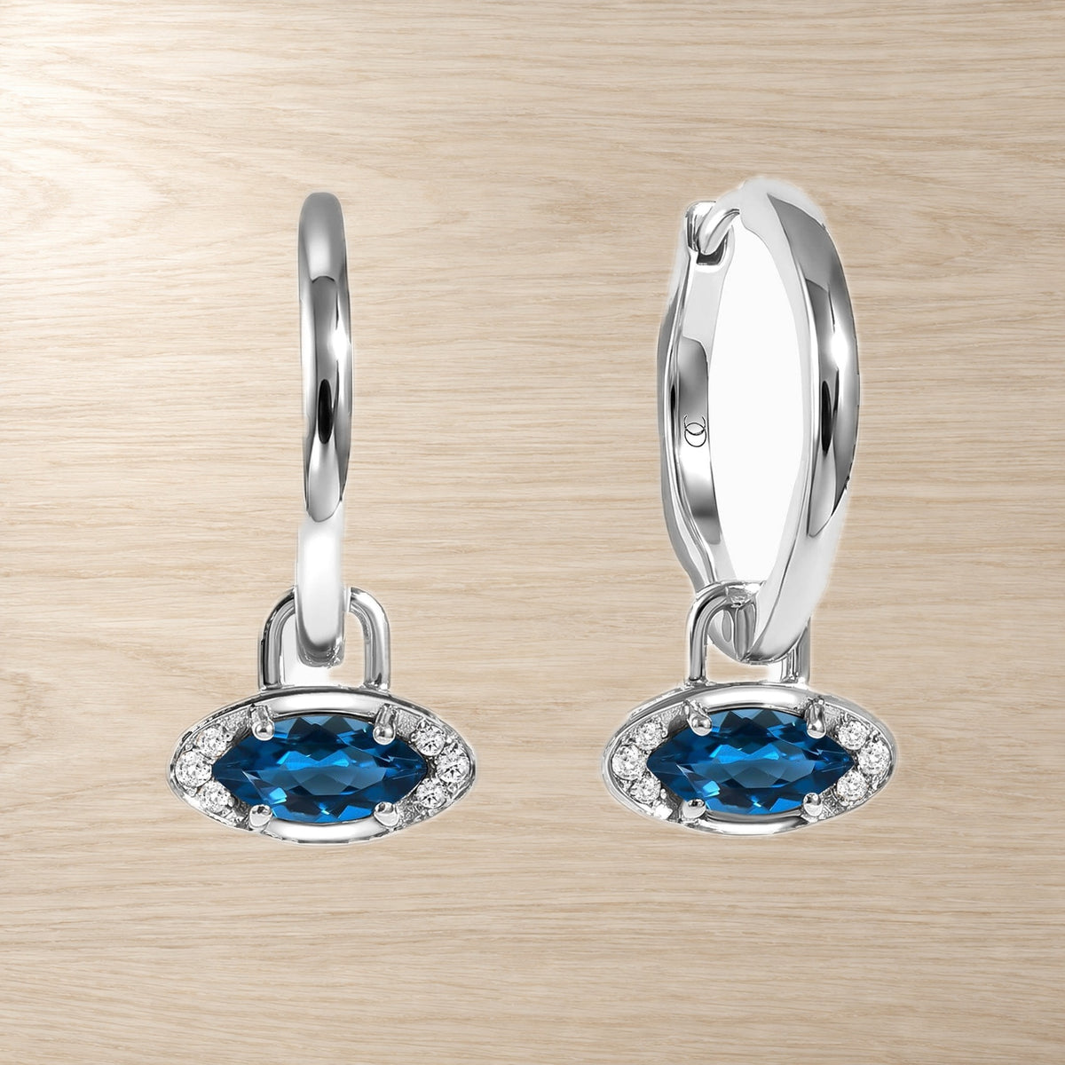 Pair of hoop earrings with blue topaz evil eye charms, shown side by side on pale wood