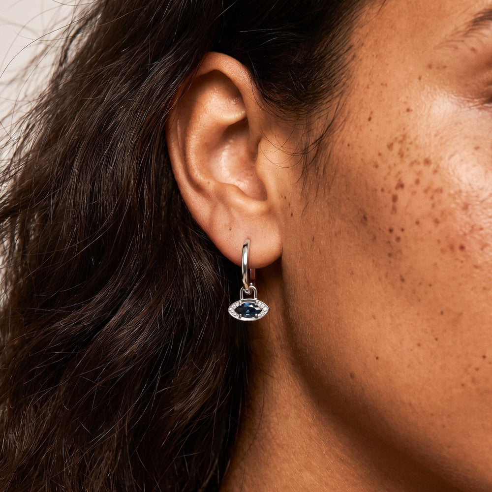 Model's ear wearing a hoop with a blue topaz evil eye charm