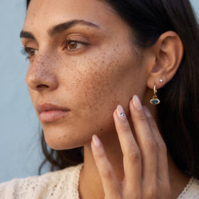Model's face in profile wearing a hoop with an evil eye charm