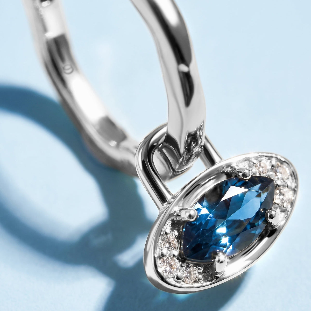 Hoop with a blue topaz evil eye charm close-up on a blue background