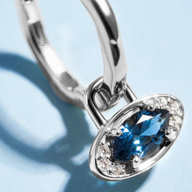 Hoop with a blue topaz evil eye charm close-up on a blue background