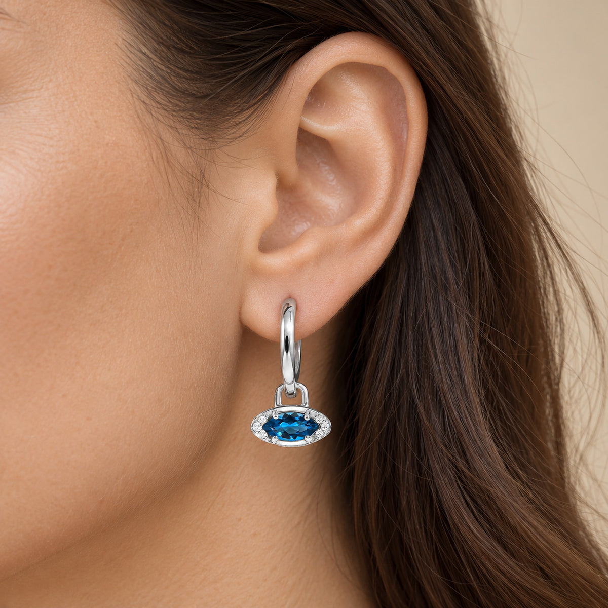 Close-up of a blue topaz evil eye hoop against a model's skin
