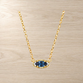 Blue topaz evil eye necklace with its chain stretched across a pale background