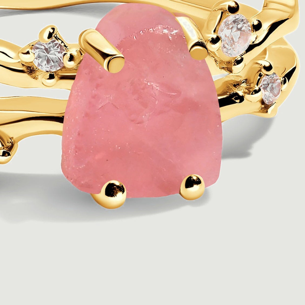 A close view shows the natural surface of the pink rose quartz beside polished yellow gold prongs and clear round stones.