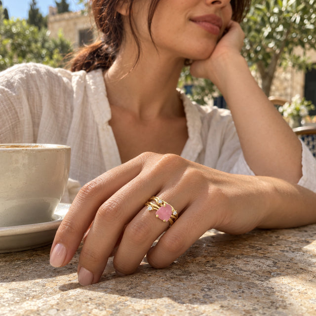 A woman wears a yellow gold rose quartz ring while resting her hand beside a ceramic cup on an outdoor cafe table.