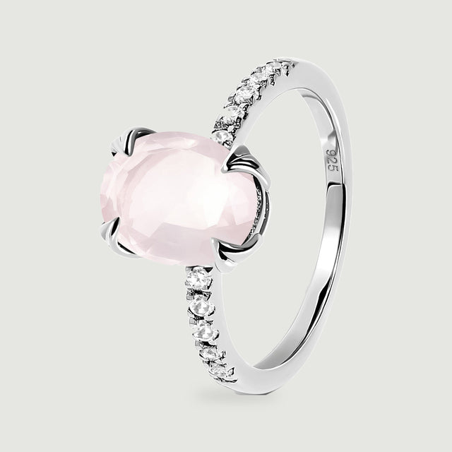 An upright sterling silver ring reveals its oval pink stone, curved band and open setting from an angled view.