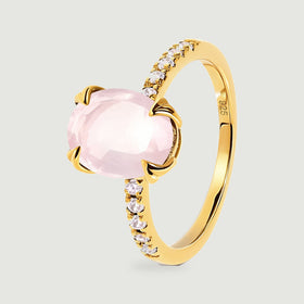 An angled yellow gold vermeil ring shows the raised pink gemstone and a row of clear accent stones.