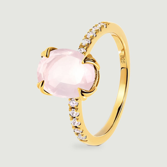 An angled yellow gold vermeil ring shows the raised pink gemstone and a row of clear accent stones.