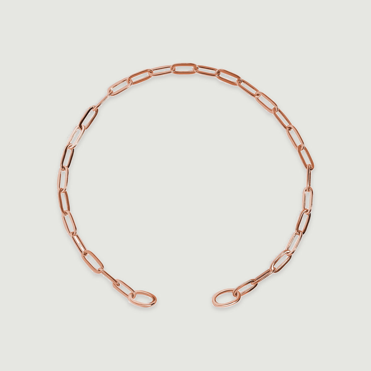 A rose gold chain bracelet forms an open oval on a light gray surface.